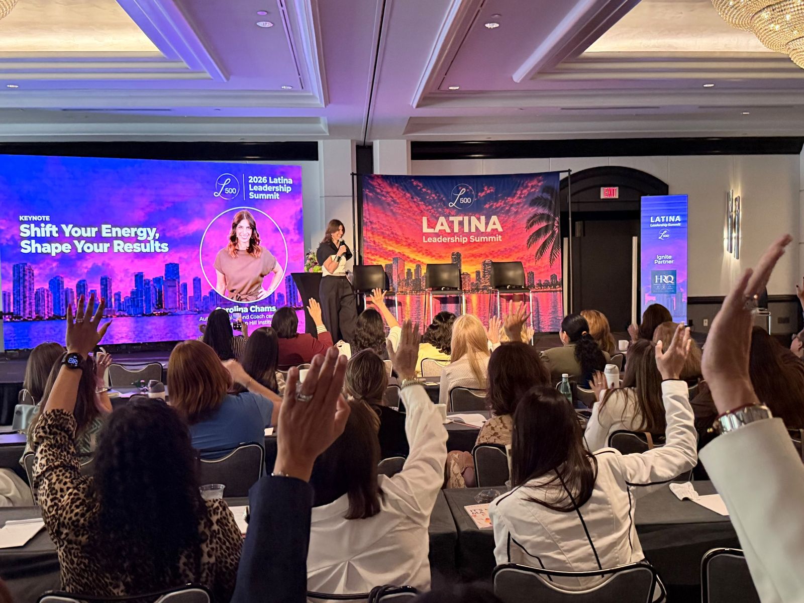 Carolina Chams dando su keynote en el L500 Latina Leadership Summit 2026, con el público levantando las manos